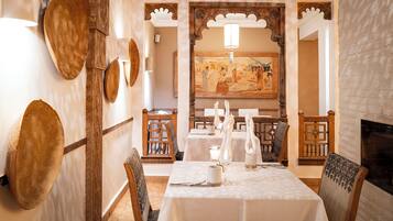 Un comedor con una mesa dispuesta para dos personas, rodeada de sillas de madera tradicionales y una pared decorativa con sombreros tejidos.