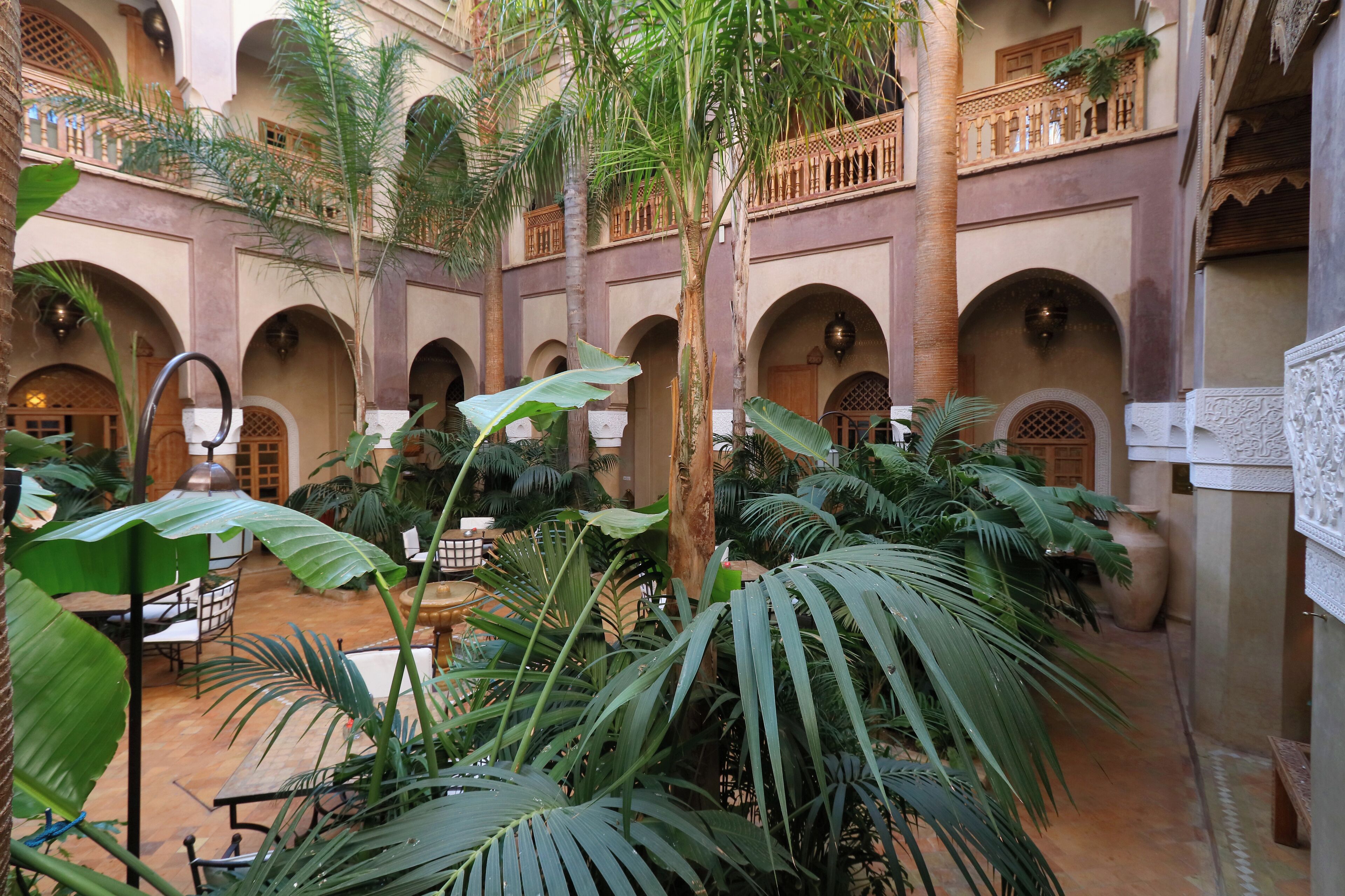 A courtyard with arches, palm trees, and a seating area.