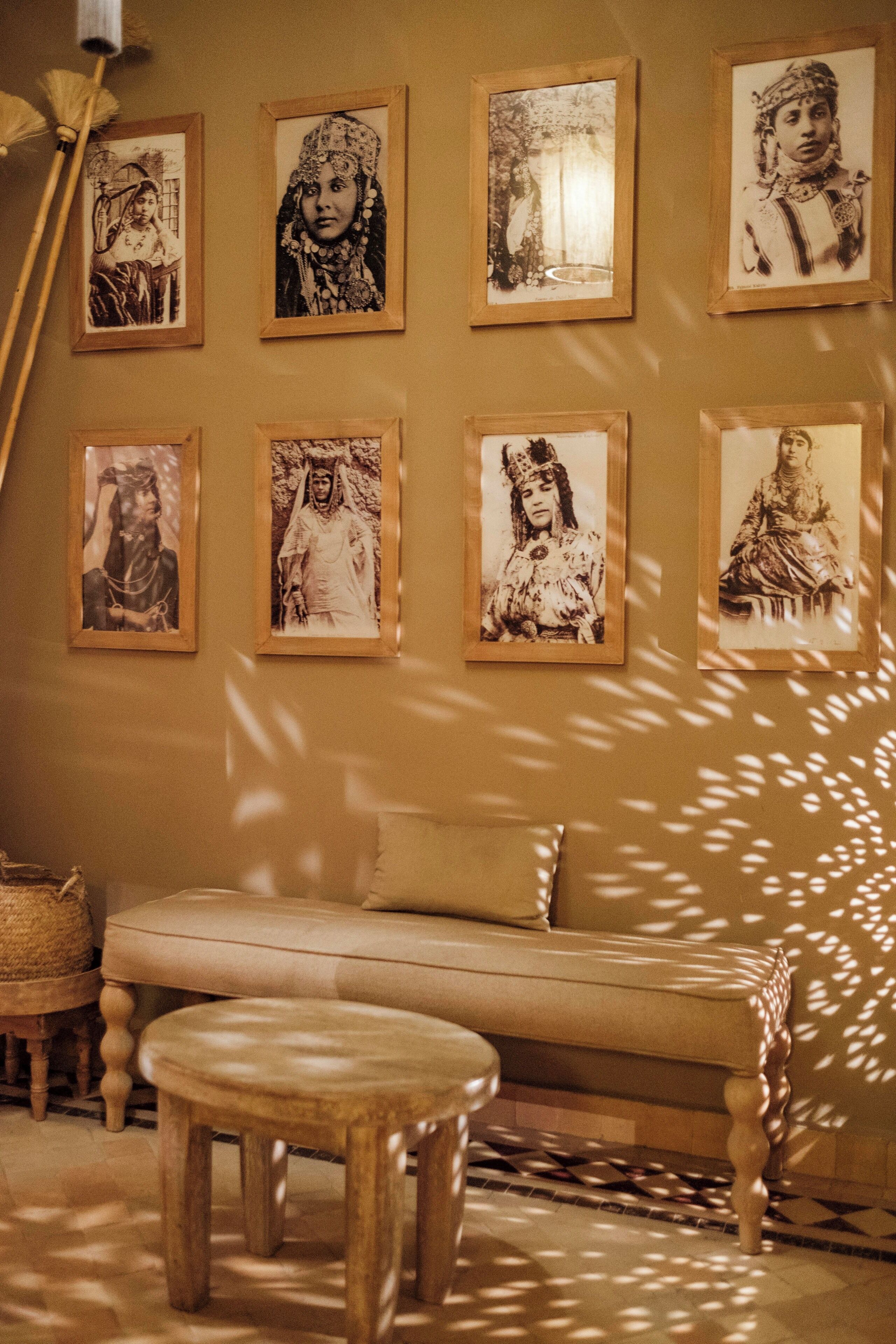 A room with a sofa and a small stool, a wall with framed pictures, and a floor lamp.
