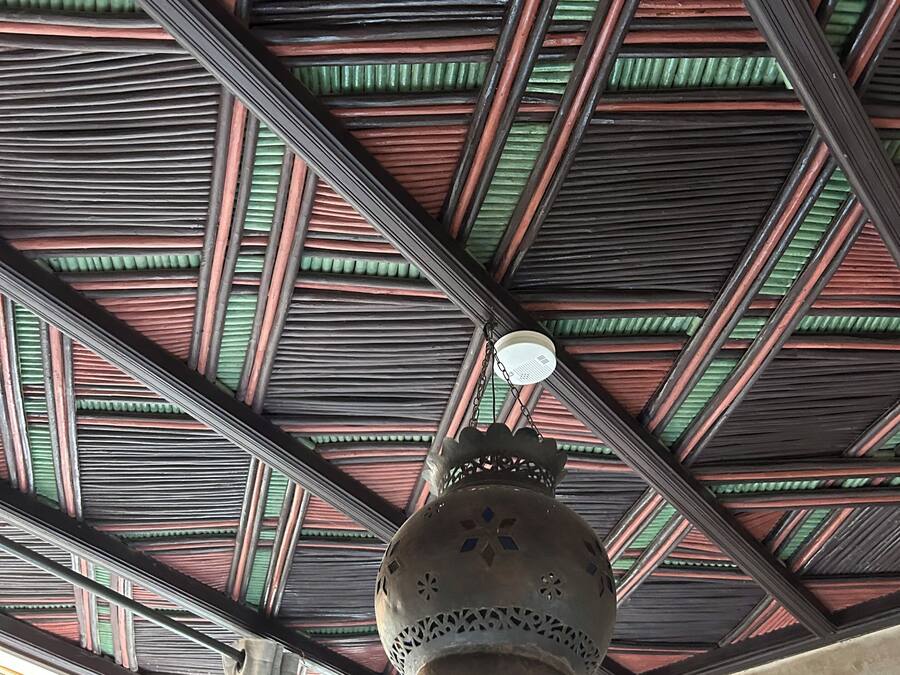 Teto com padrão geométrico de vigas de madeira e um candeeiro pendente.