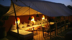 A tented outdoor seating area with a sofa, chairs, and tables, illuminated by hanging lamps. - Dar Touyir (Marrakech)
