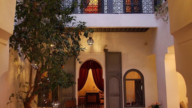 An indoor courtyard with a dining area, a tree, and a balcony with a railing. - Dar Touyir (Marrakech)