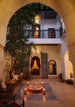 An indoor courtyard with a dining area, a tree, and a balcony with a railing. - Dar Touyir (Marrakech)