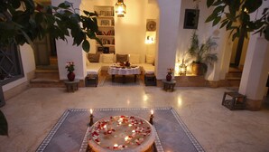A cozy lounge area with a circular seating arrangement, a small table with a vase of flowers, and a bookshelf in the background. - Dar Touyir (Marrakech)