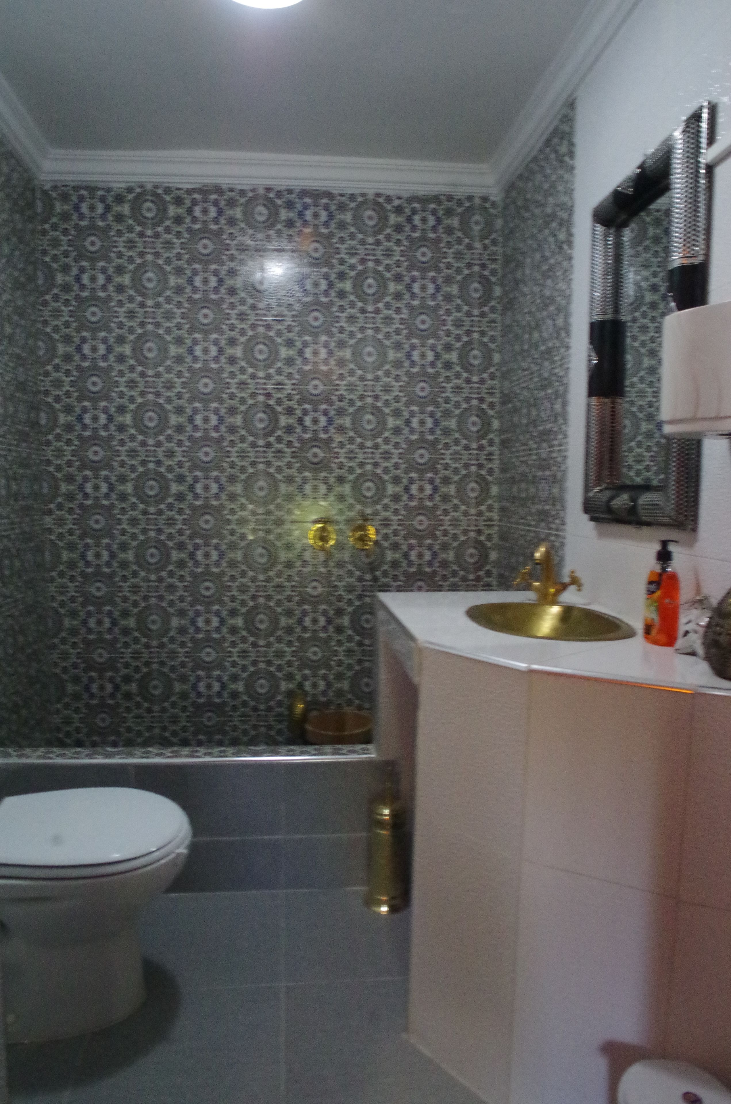 A bathroom with patterned tiles, a white toilet, a sink with a gold faucet, and a mirror above the sink.