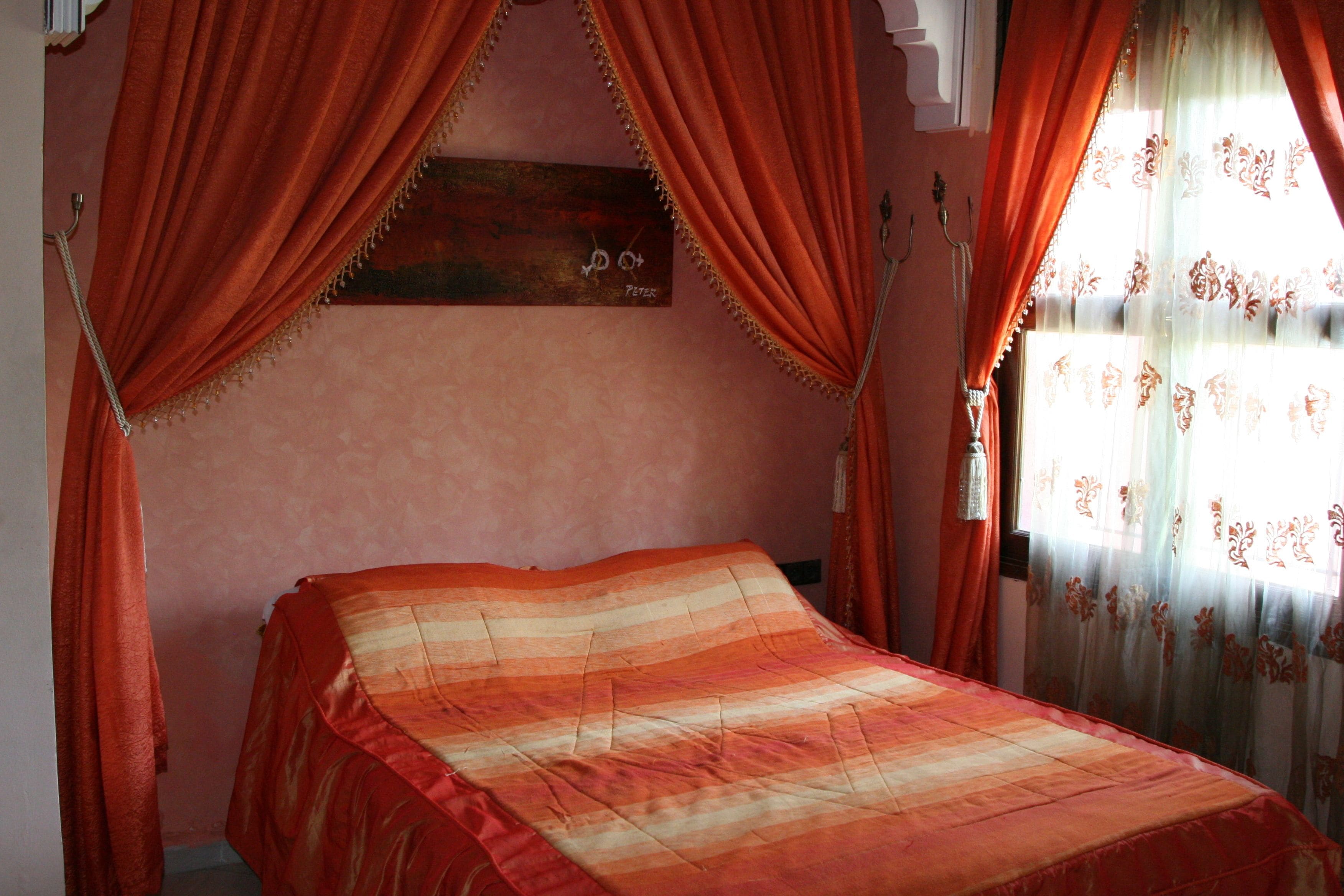 A bedroom with a bed, red curtains, and a wooden headboard with a nameplate.