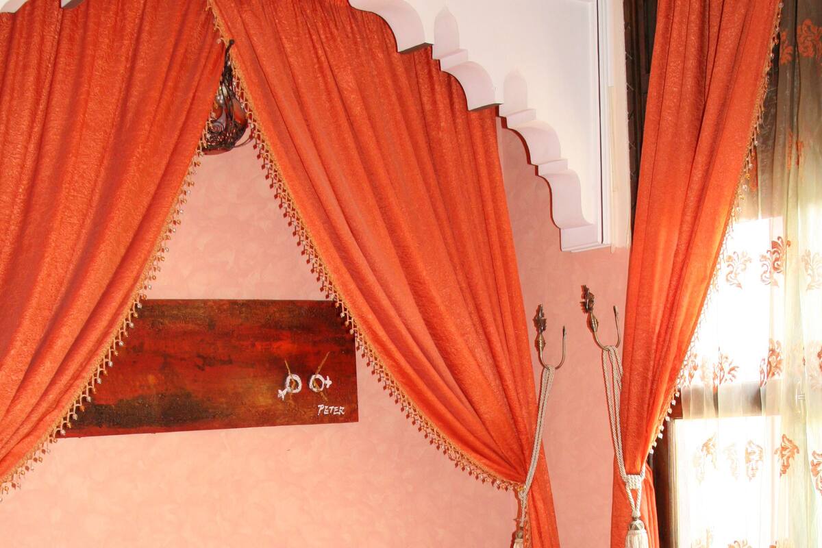 Una cama con colcha a rayas, cortinas naranjas y cabecera de madera.