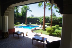 Un patio coperto con piscina, palme e vista su un rigoglioso giardino.