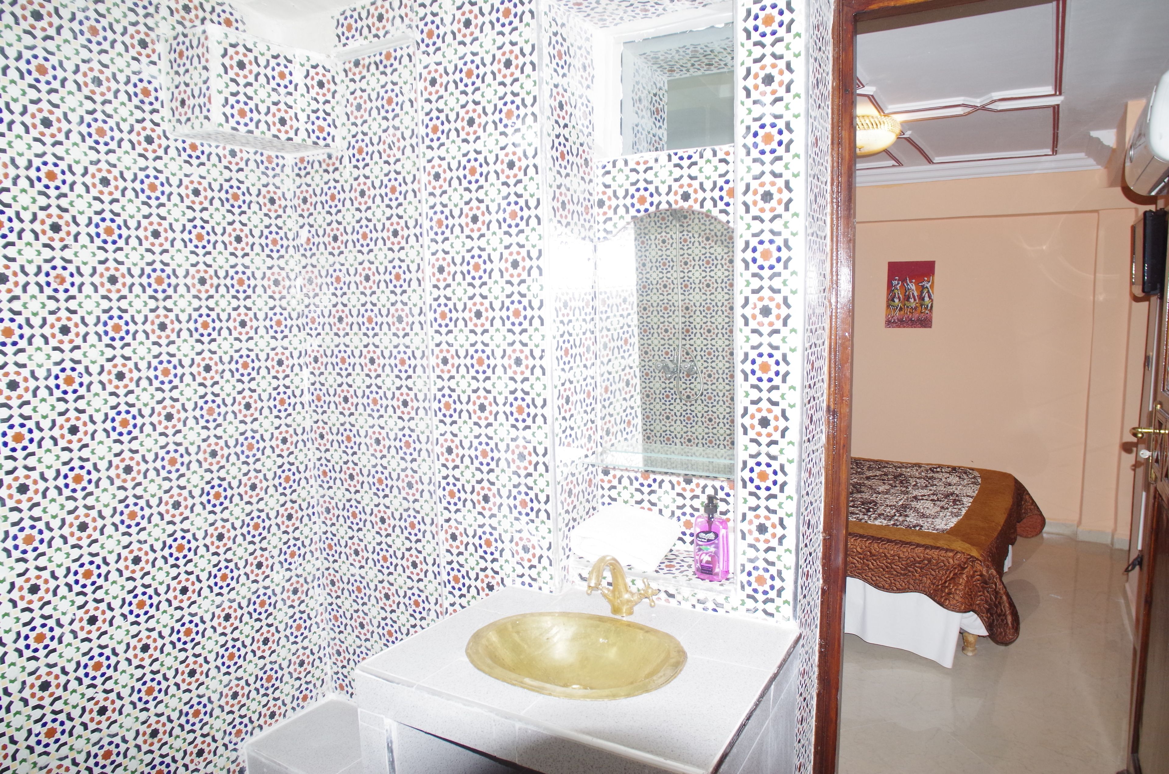 A bathroom with a patterned tile wall, a sink with a gold faucet, and a mirror above it.