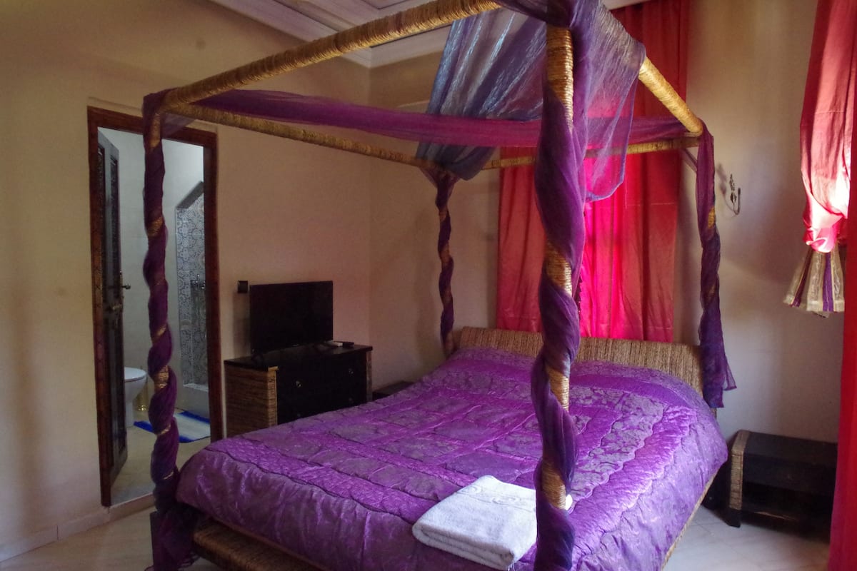 Una cama con dosel con un edredón morado y una toalla blanca encima.