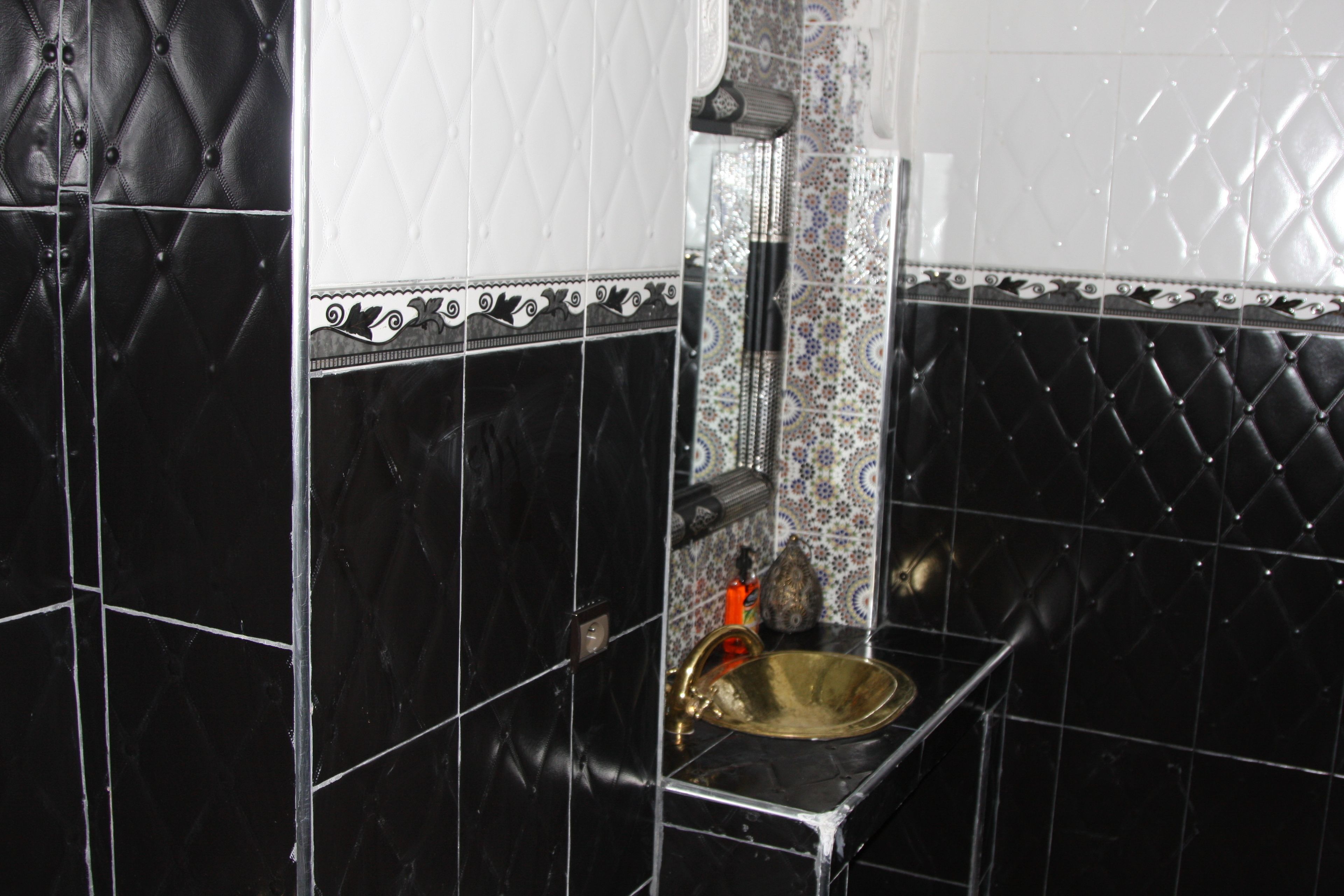 A bathroom with black and white tiled walls, a gold sink, and a mirror.