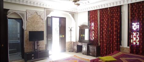Quarto tradicional com cama, televisão e uma janela grande com cortinas.