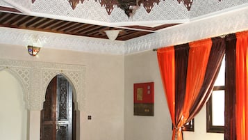 A living room with a brown leather sofa, orange cushions, and a patterned ceiling.