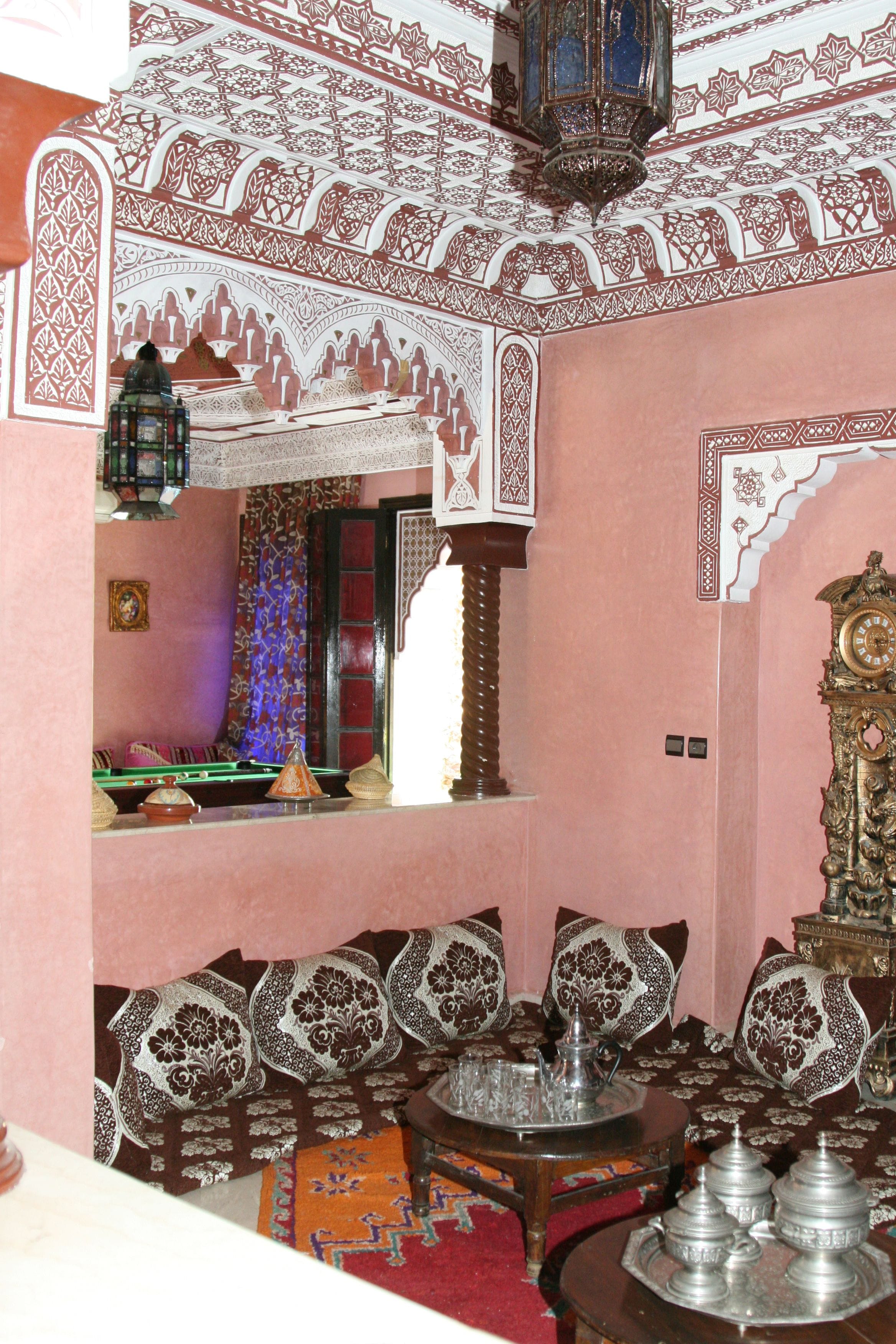 A traditional room with intricate wall and ceiling designs, a large ornate clock, and a seating area with cushions and a small table.