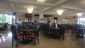 Un'ampia sala da pranzo con diversi tavoli e sedie, grandi finestre e lampadari.