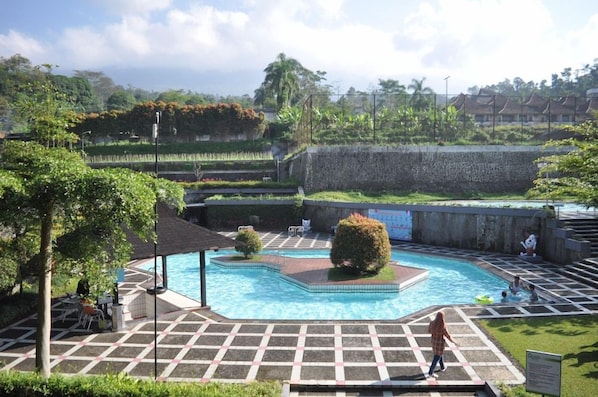 Area piscina con solarium piastrellato, zona relax coperta e vista su una zona residenziale sullo sfondo.