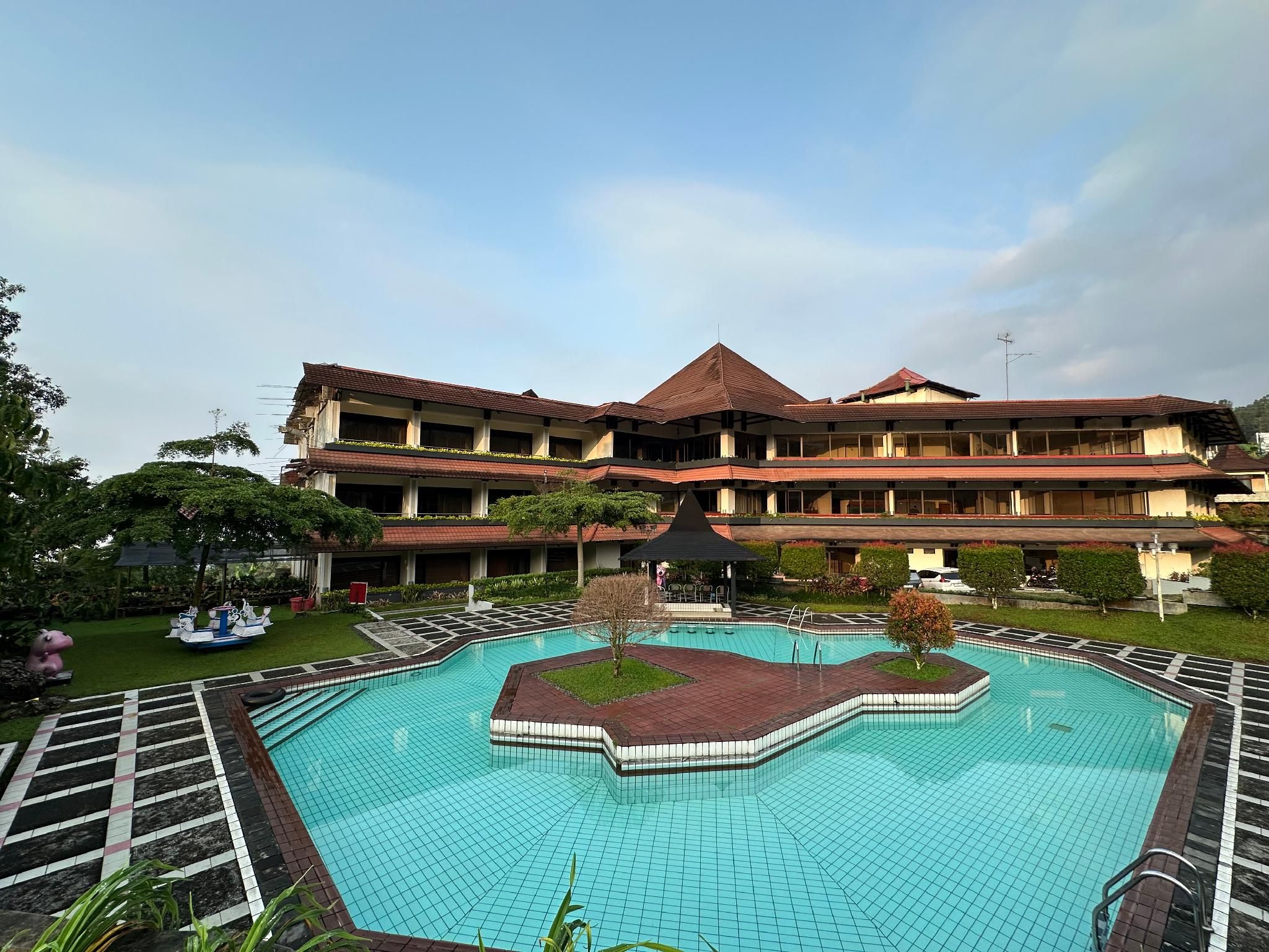 A hotel with a large swimming pool, multiple balconies, and a garden area.