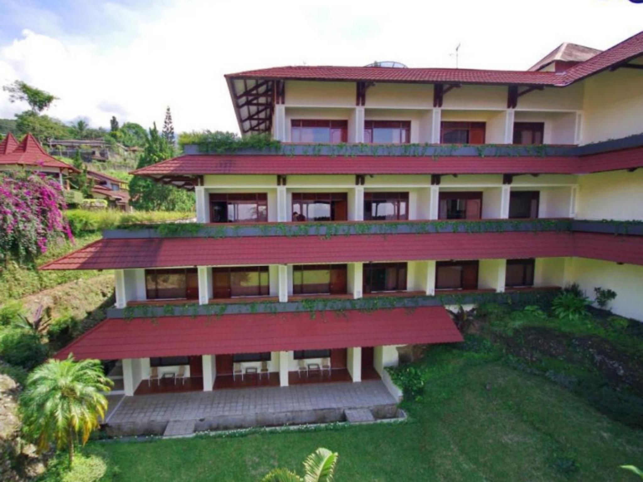 A multi-story hotel with balconies, a flat roof, and a garden area.