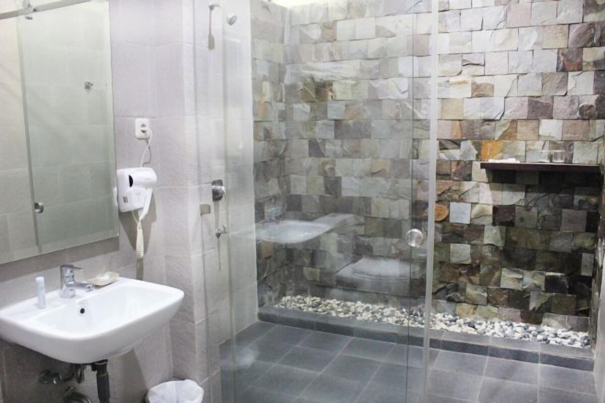A bathroom with a glass shower enclosure, a sink, and a stone wall.
