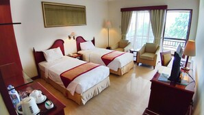 A hotel room with two beds, a sitting area with a chair and table, a balcony with curtains, and a coffee station. - Le Dian Hotel (BANTEN)