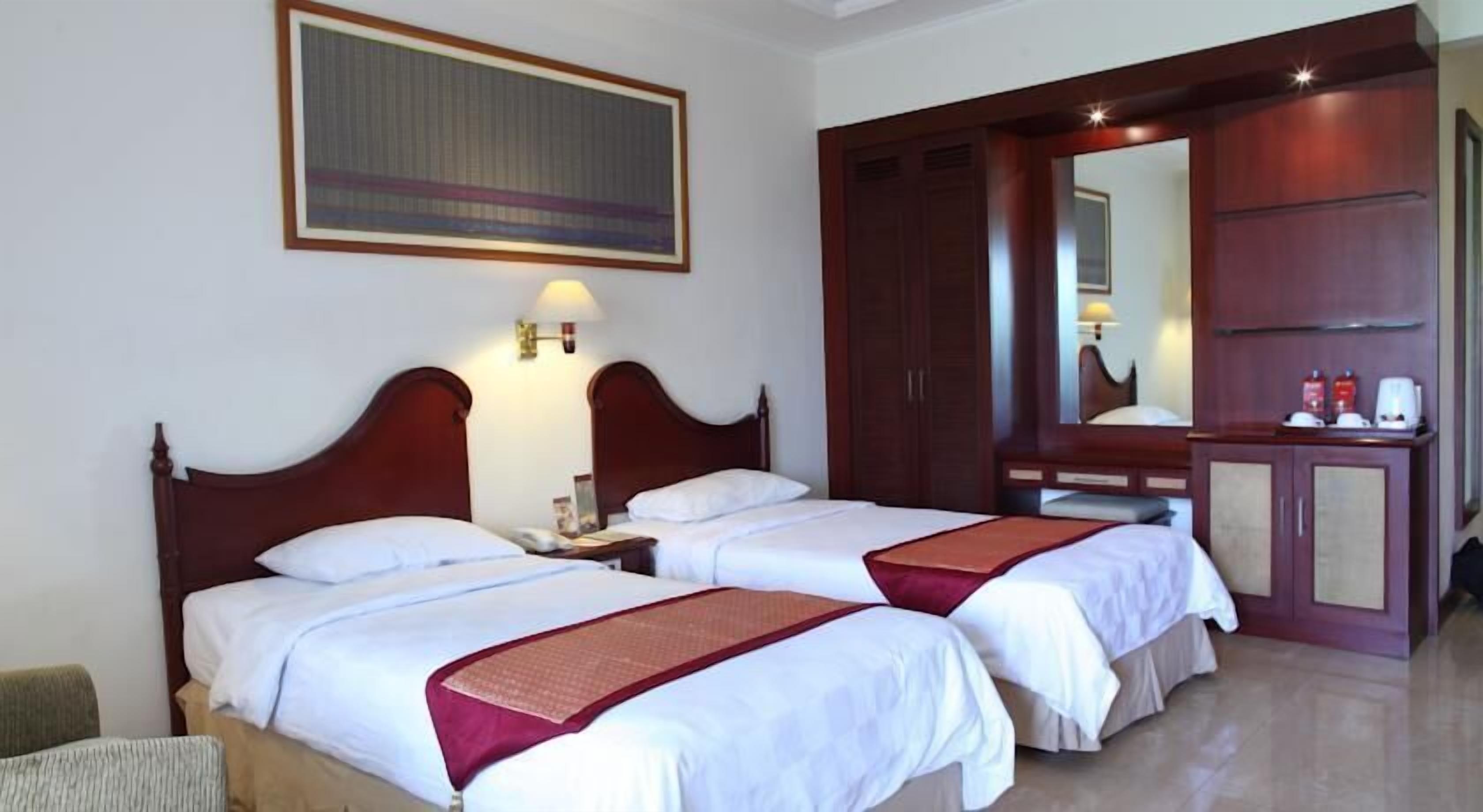 A hotel room with two beds, a large mirror, a wardrobe, and a painting on the wall.