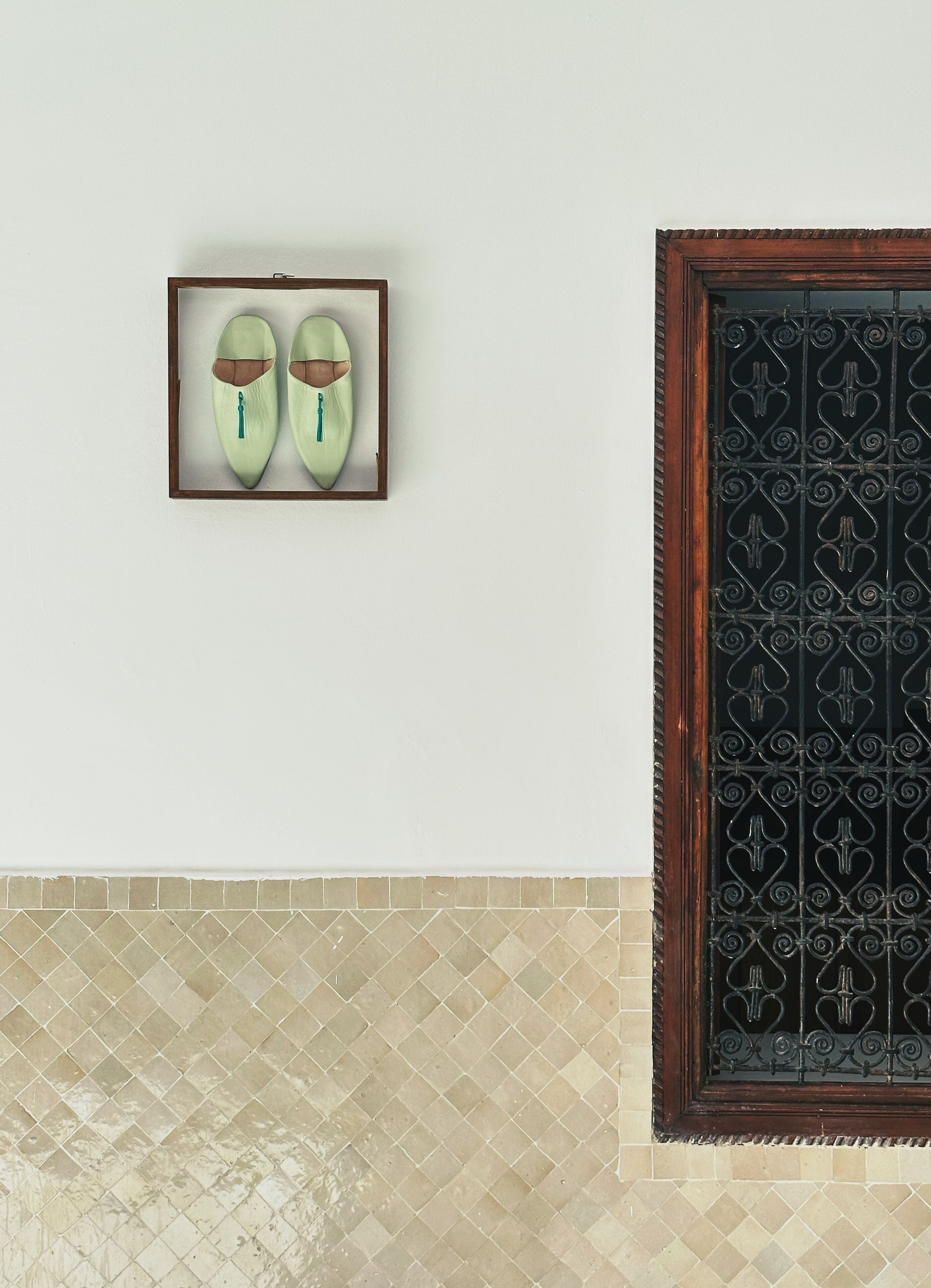 A framed pair of shoes on a wall, a decorative metal gate, and a patterned tile floor.