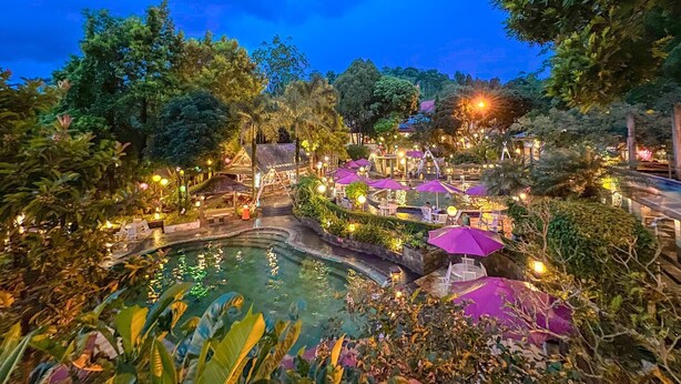 Een resort met een zwembad, terras buiten en weelderige begroeiing.