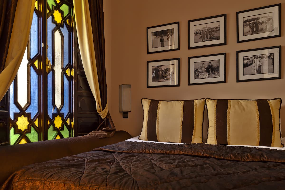 A bedroom with a bed, a nightstand, and a wall-mounted lamp. There are four framed photographs on the wall.