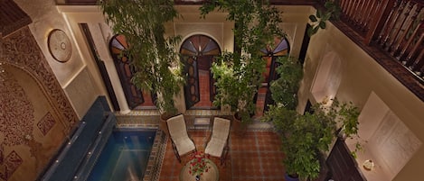 An indoor courtyard with a pool, two chairs, and potted plants.
