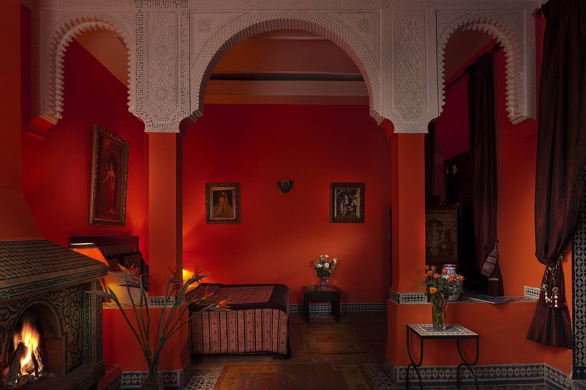 A room with red walls, a bed, a fireplace, and decorative arches.