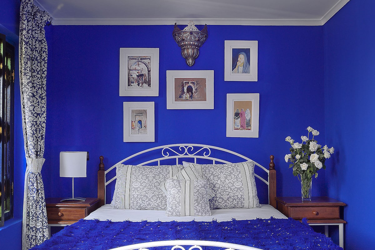A bedroom with a blue wall, a white ornate ceiling, and a bed with a blue bedspread.