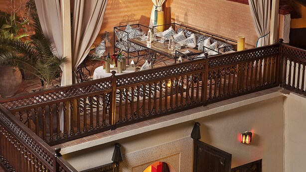 Una terraza en la azotea con zona de comedor, una mesa dispuesta para dos personas, rodeada por una barandilla decorativa.