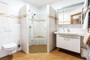 A modern bathroom with a glass shower enclosure, a white toilet, a sink with a mirror, and wooden flooring. - Hotel Fv Rst (Unterweissenbach)