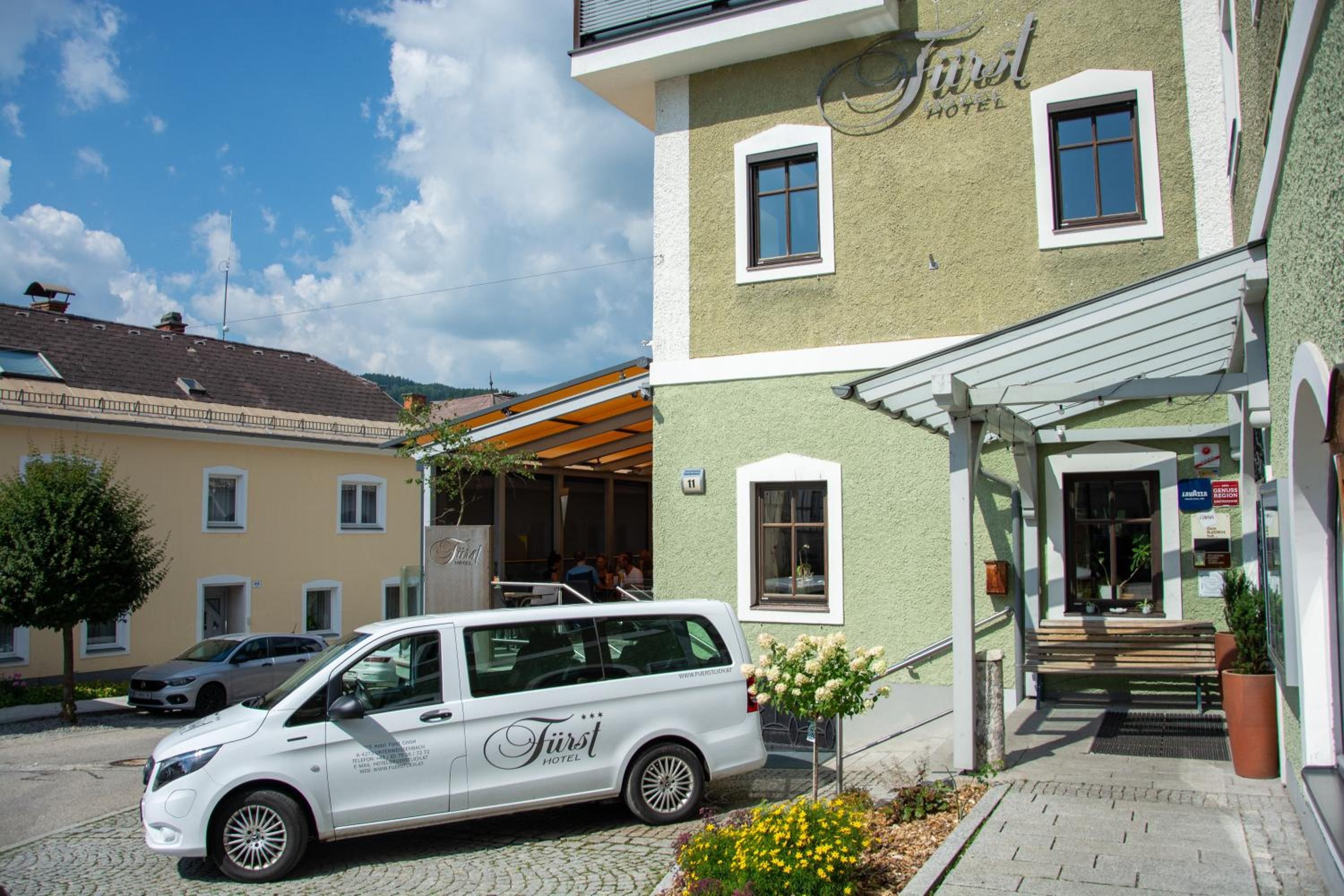 A white van parked in front of a building with a sign that reads 'First Hotel.'