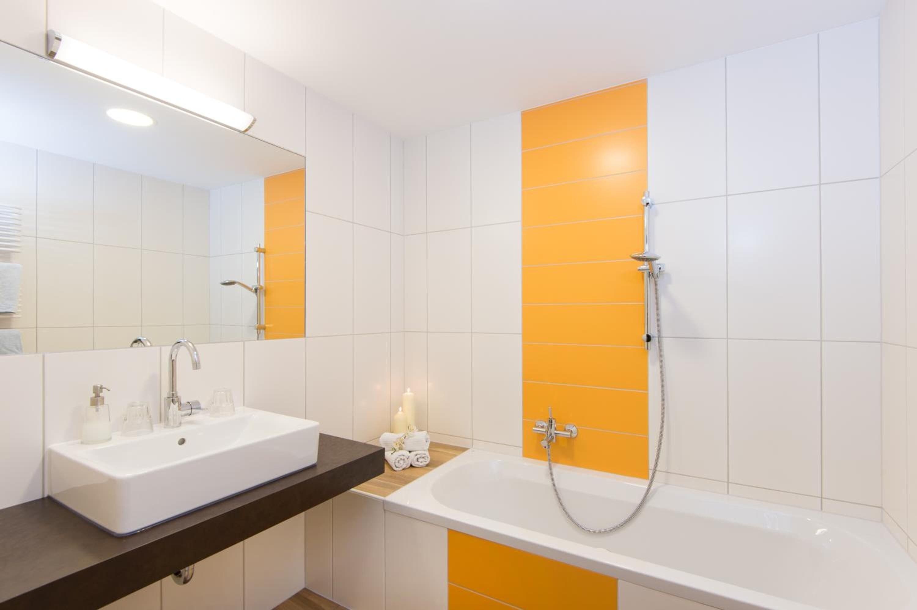A modern bathroom with a white sink, a mirror, and a shower with orange tiles.