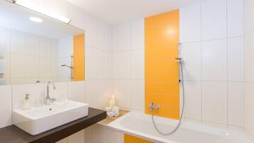 A modern bathroom with a white sink, a mirror, and a shower with orange tiles.