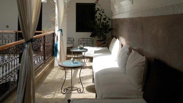 A room with a white sofa, a small table, and a decorative hanging light. There is a balcony with a railing and a view of the outside. - Riad Ailen (Marrakech)