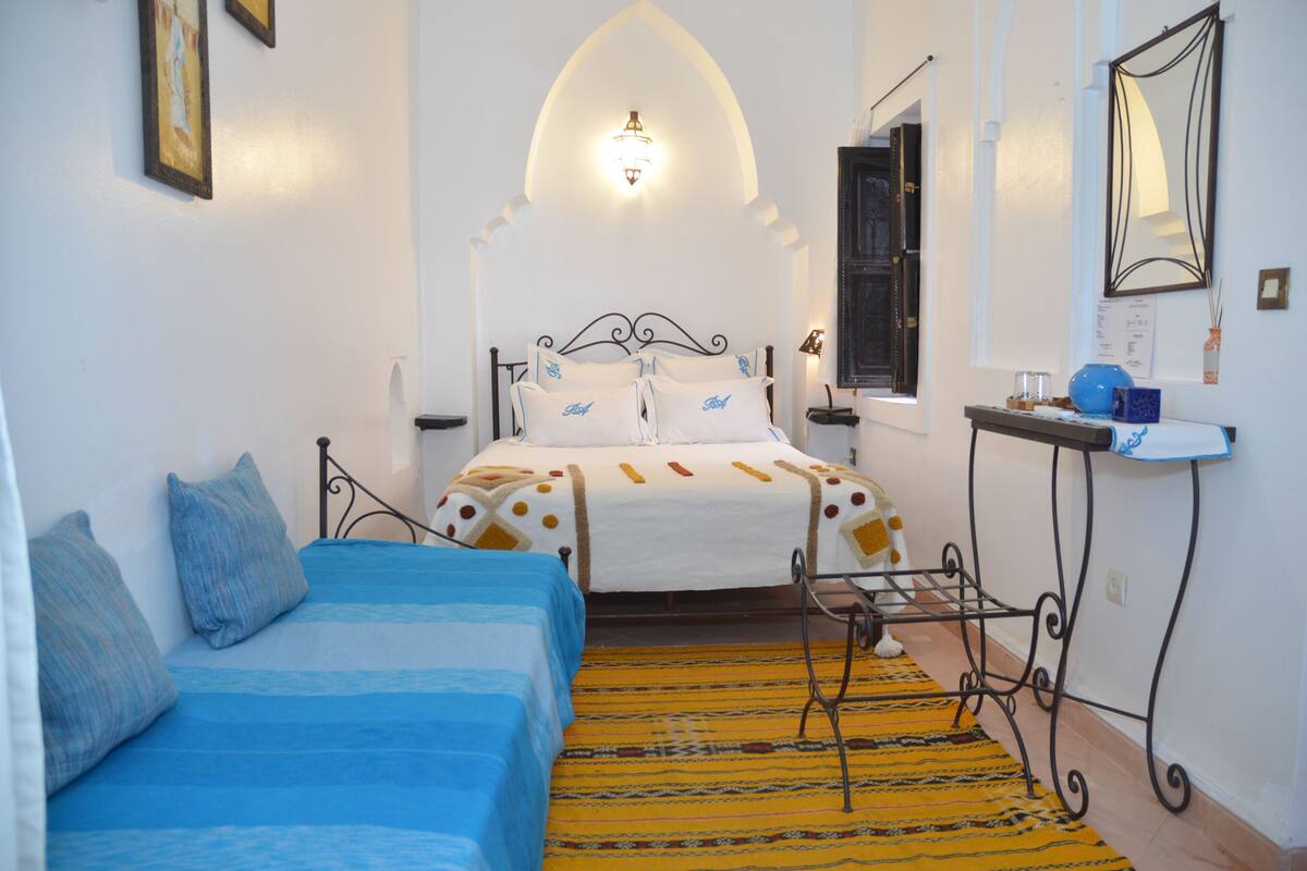 Un dormitorio con cama, sofá, una mesita y un espejo.