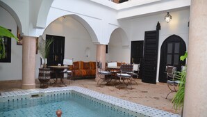 A pool area with a tiled floor, a seating area with chairs and a sofa, and a large black door. - Riad Ailen (Marrakech)
