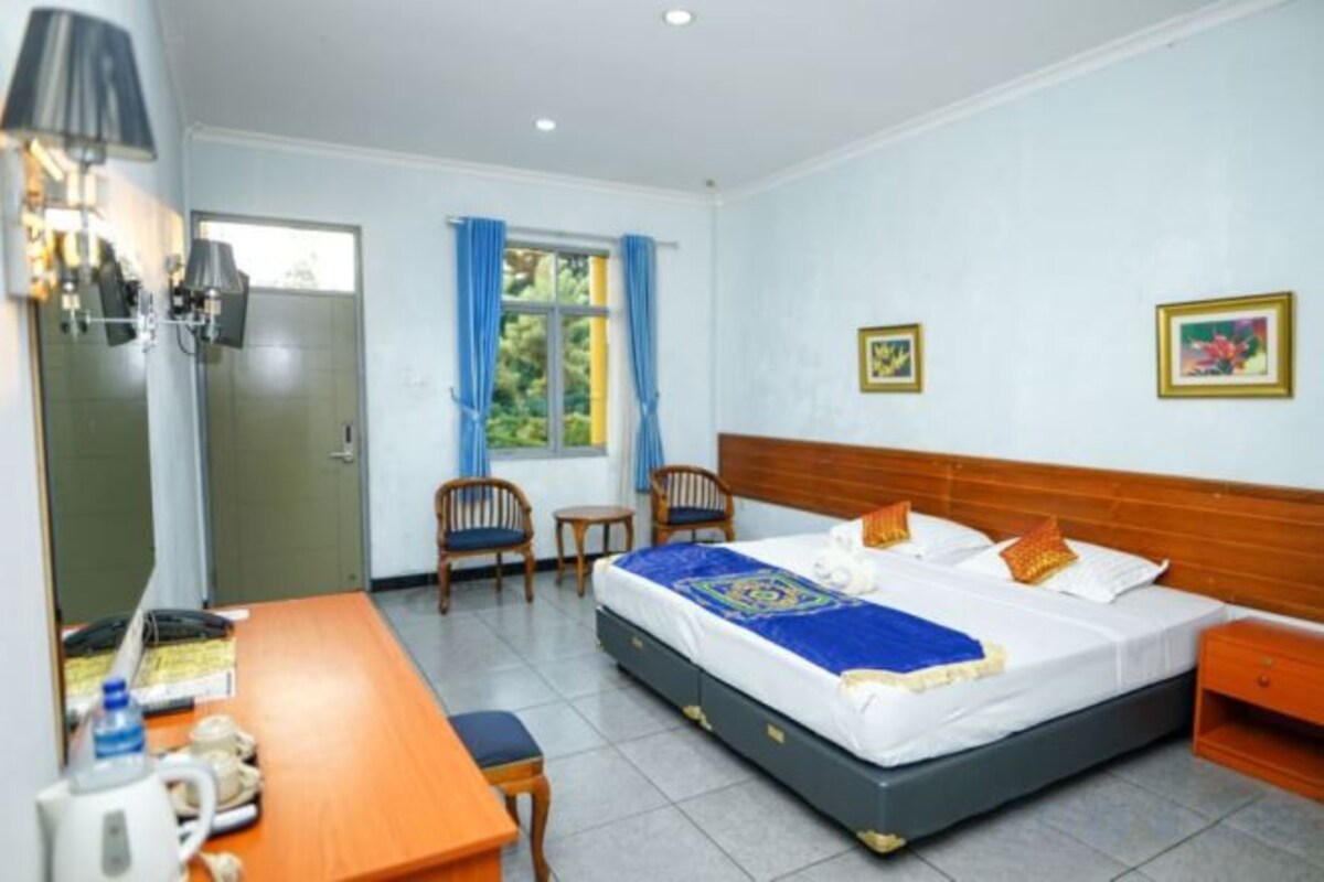 Une chambre d’hôtel avec un lit, un bureau, une chaise, une table de chevet et une fenêtre avec des rideaux.
