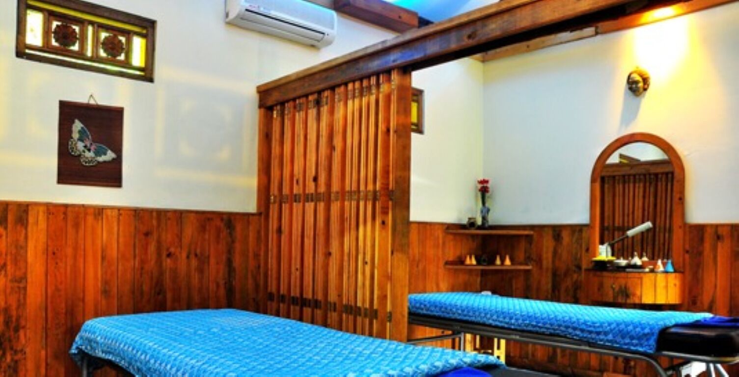 A room with wooden paneling, two beds with blue bedding, a mirror, and a shelf with toiletries.