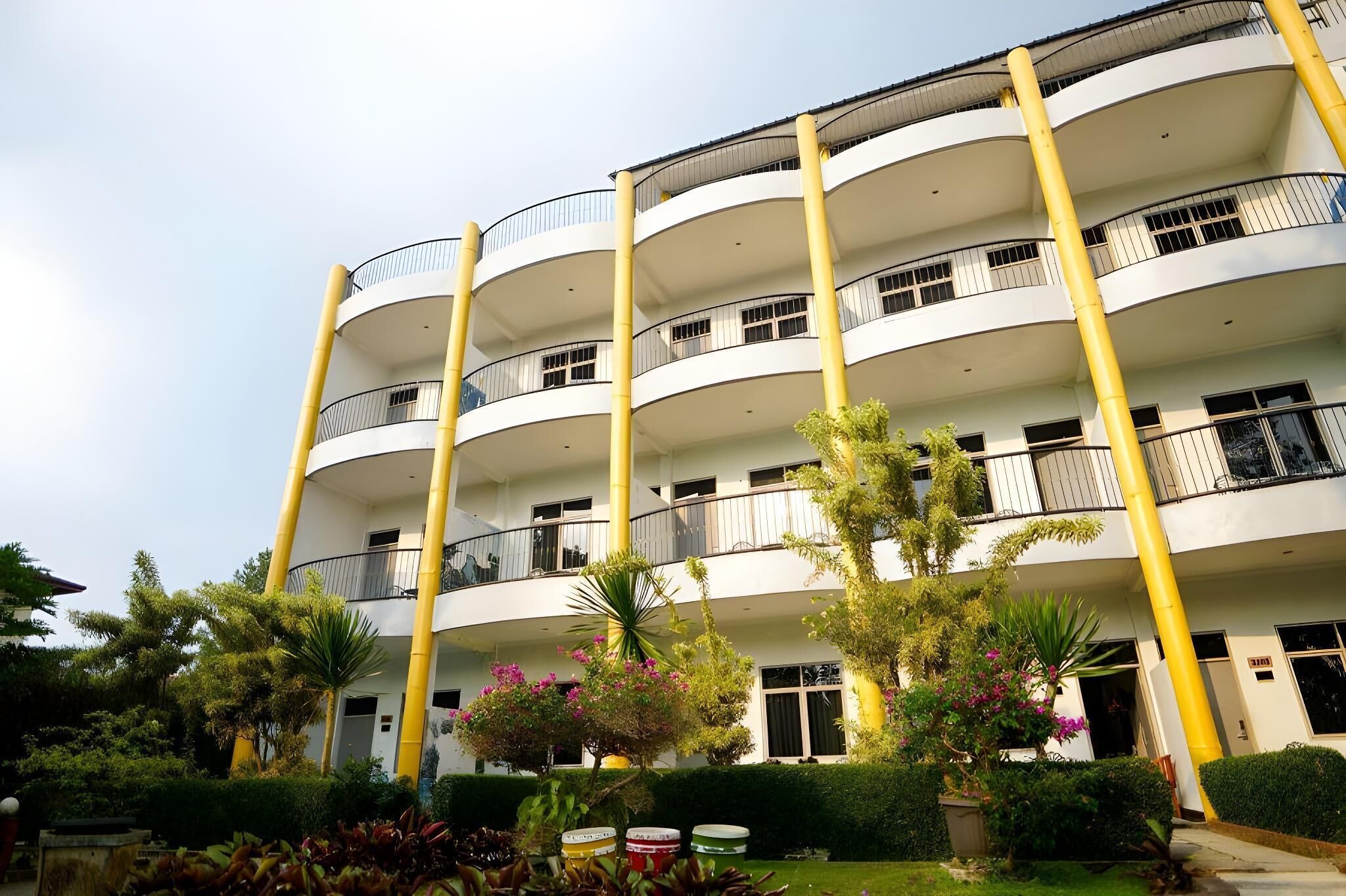 A multi-story building with balconies and a garden area with various plants and flowers.