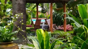 A tropical garden with a gazebo, wooden chairs, and a bird feeder. - Taman Sari Hotel Dan Resort (Sukabumi)