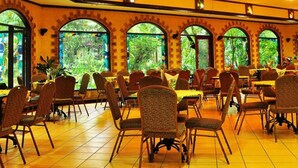 A spacious dining area with multiple tables and chairs, large arched windows with a view of greenery, and a high ceiling with recessed lighting. - Taman Sari Hotel Dan Resort (Sukabumi)