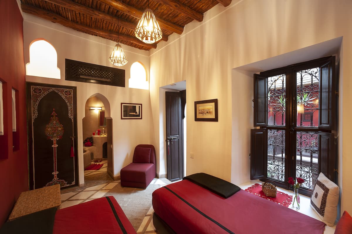A hotel room with two beds, a sitting area, and a view of a red building through a window.