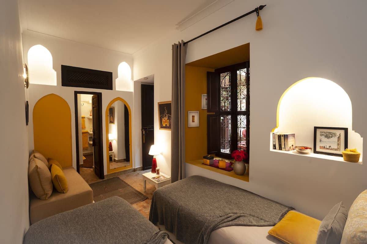 A cozy hotel room with two beds, a sitting area, and a window with decorative items.