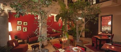 A cozy indoor setting with a red wall, a dining area with a table set for two, and a comfortable seating area with a sofa and chairs.