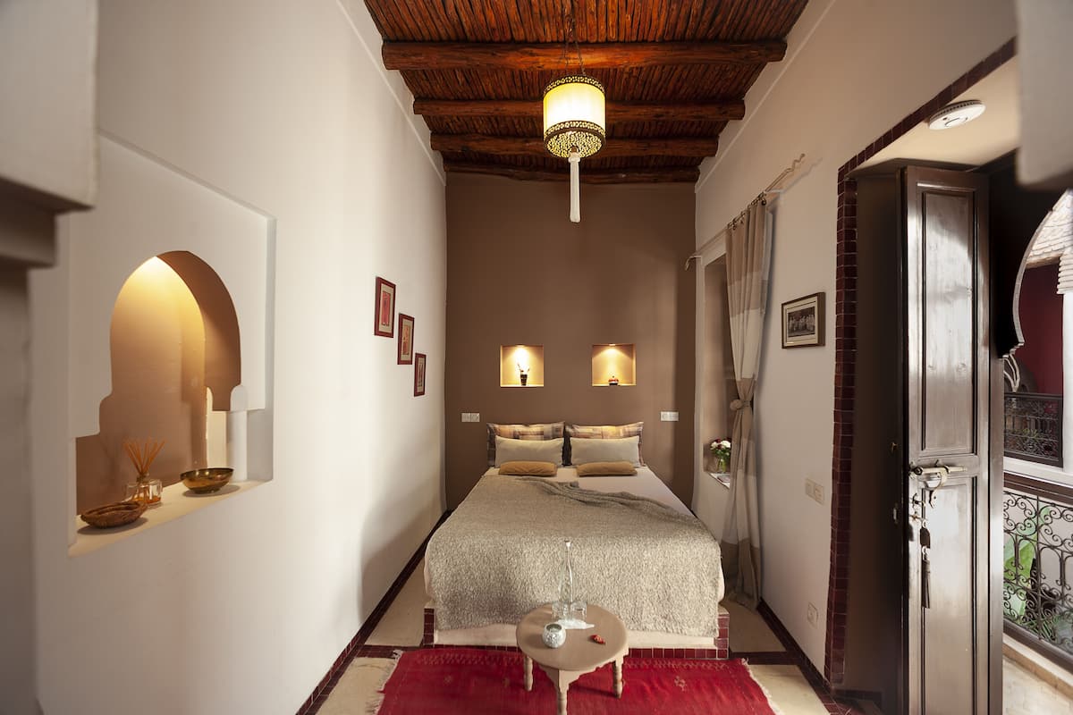 A narrow hallway leading to a bed with a wooden ceiling and two wall-mounted lamps.