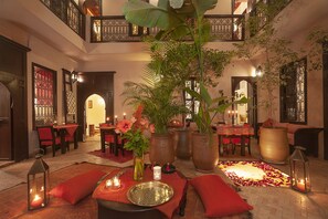A spacious lobby with a high ceiling, multiple dining areas, and a central seating area with a decorative rug and candles. - Riad Boussa (Marrakech)
