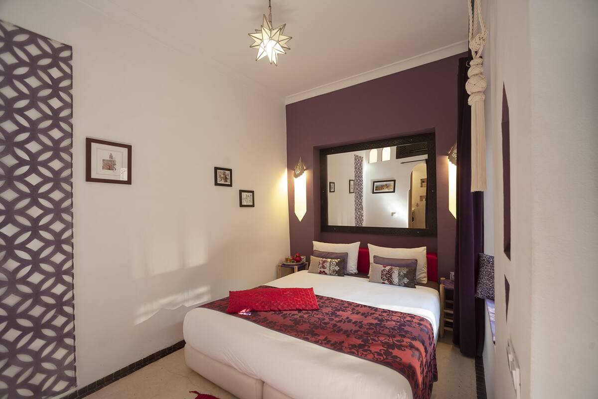 A bedroom with a bed, a nightstand, a mirror, and a patterned wall.